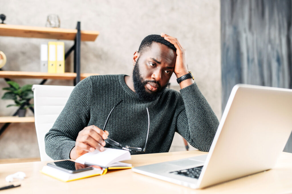 a man with his head in his hand scowling at his office laptop computer