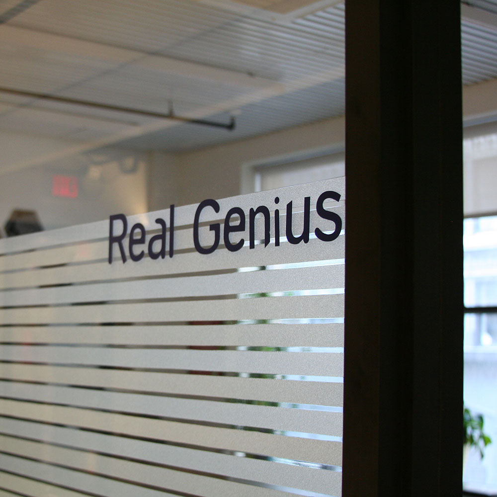 an interior glass wall at the office with 'Real\l Genius' stenciled on
