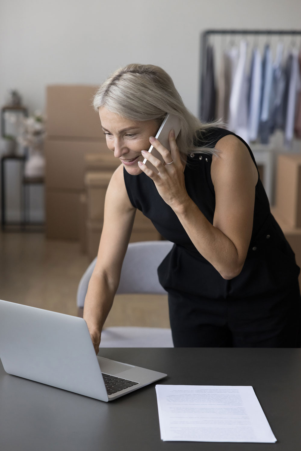 Cheerful senior small online business owner looking at her laptop while she's on the phone